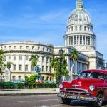 Old classic American maroon car rides in front of the Capitol. Before a new law issued on October 2011, cubans could only trade cars that were on the road before 1959.